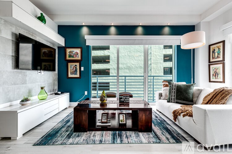 A modern living room with a white sofa, a wooden coffee table, and a white kitchen area.