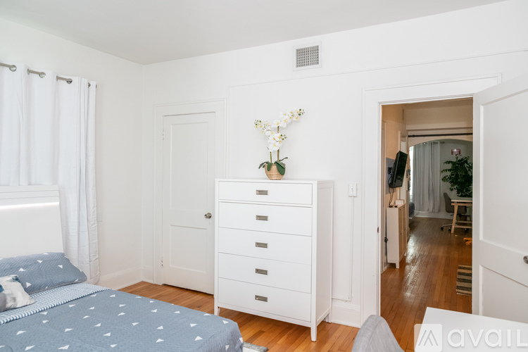 A bedroom with a bed, dresser, and a window with curtains.