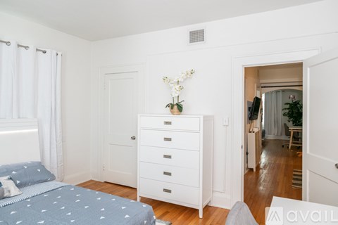 A bedroom with a bed, dresser, and a window with curtains.