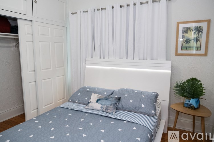 A bed with a blue and white patterned comforter sits in a room with white walls and a wooden floor.