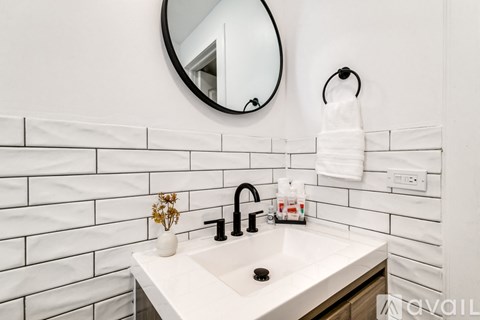 A white bathroom with a round mirror and a white sink.