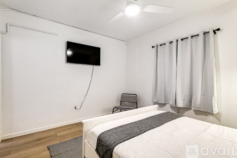 A bedroom with a bed, chair, and a flat screen TV mounted on the wall.