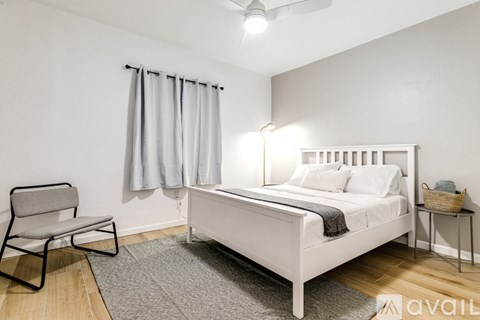 A bedroom with a white bed, grey chair, and a grey rug.