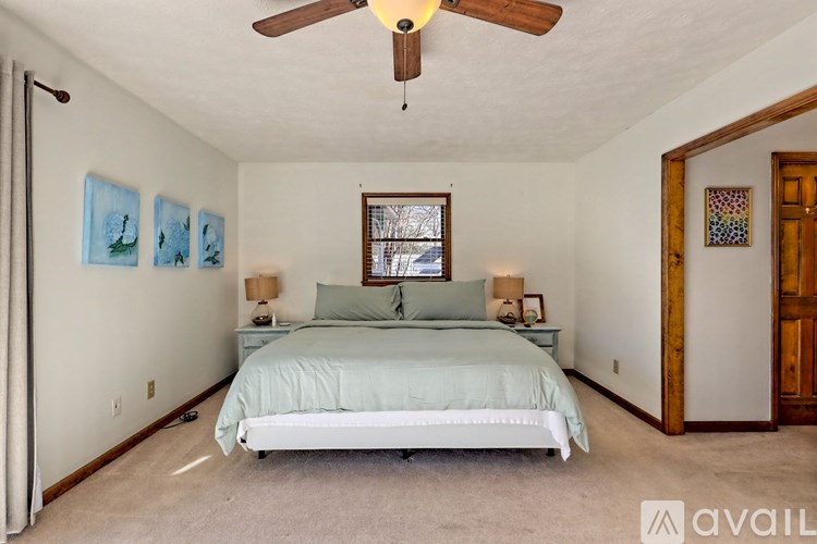 A bedroom with a bed, two lamps, a ceiling fan, and pictures on the wall.