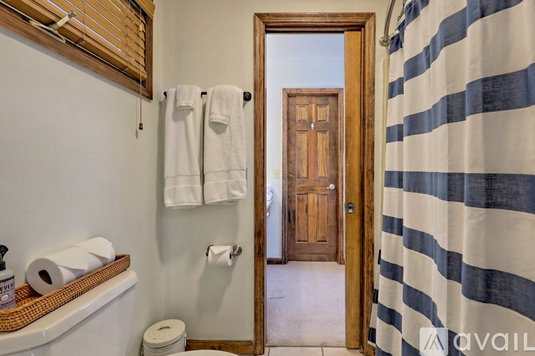 A bathroom with a toilet, toilet paper, a towel rack with towels, a wooden door, and a striped shower curtain.