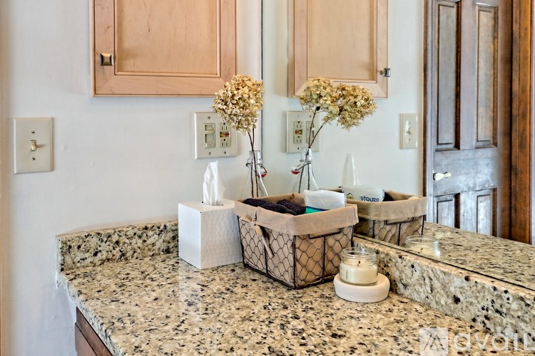 A bathroom counter with a tissue box, a candle, and two vases with flowers.