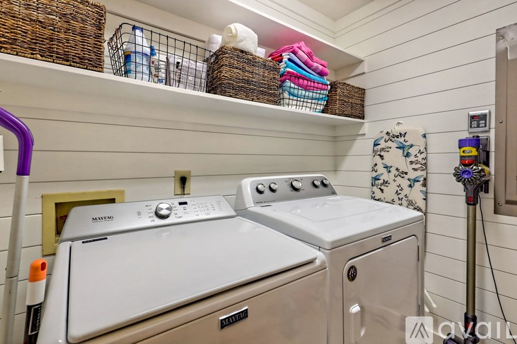 A laundry room with a washer and dryer, a basket on the shelf, and a vacuum cleaner.