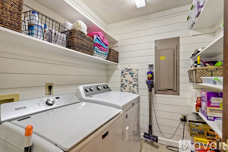 A laundry room with a washer and dryer, a vacuum cleaner, and a shelf with various items.