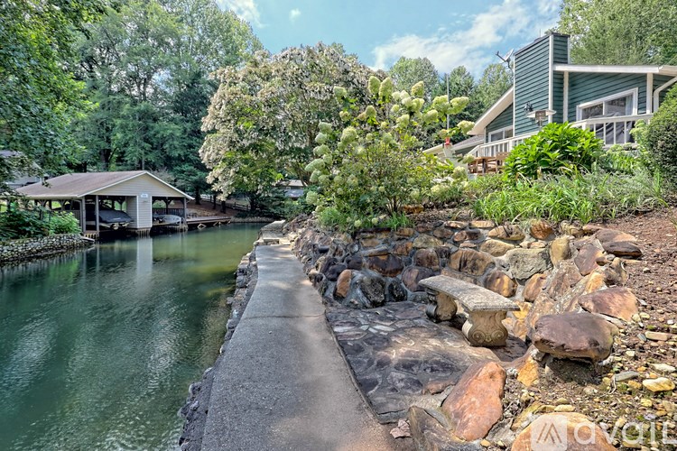 A house is situated by a body of water with a concrete walkway leading to it.