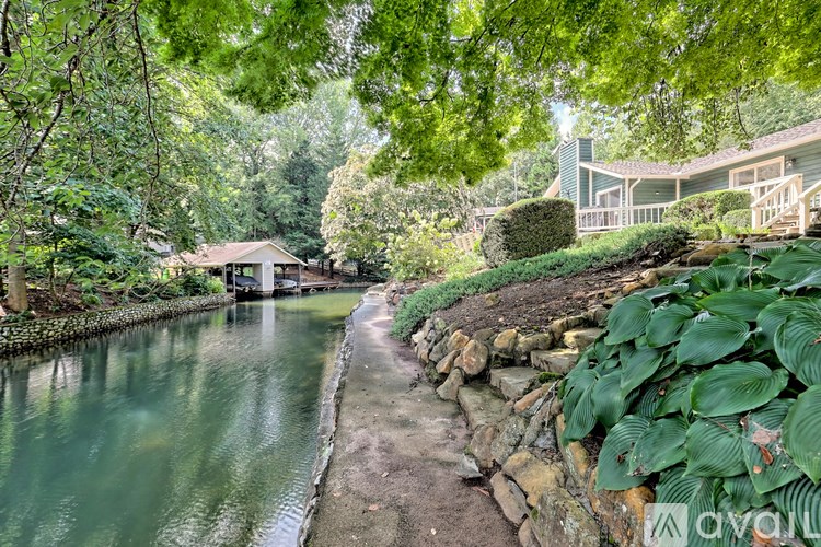 A house is situated by a body of water with a stone wall and greenery.