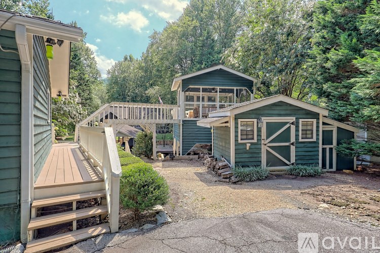 A green house with a wooden deck and a smaller green house in the background.