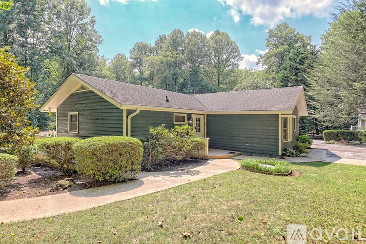 A house with a green exterior and a grey roof is surrounded by greenery.