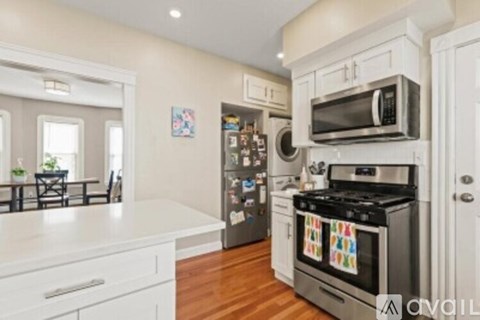 A kitchen with white cabinets and appliances, a wooden floor, and a dining area with a table and chairs.