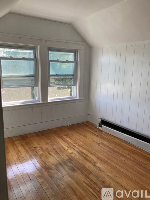A room with wooden floors and white walls has two windows.