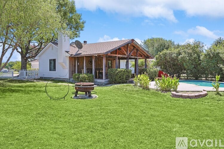 A house with a white exterior and a brown roof is surrounded by a green lawn and a pool.