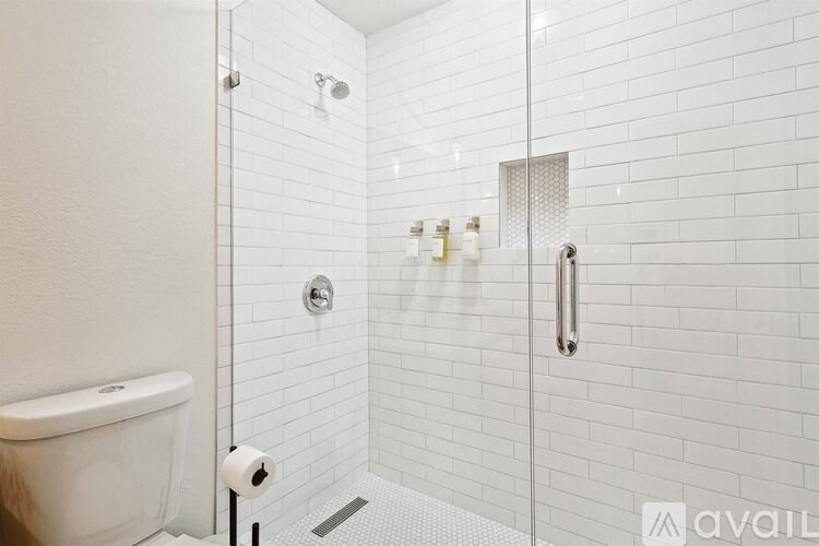 A white tiled bathroom with a toilet paper roll on the floor.