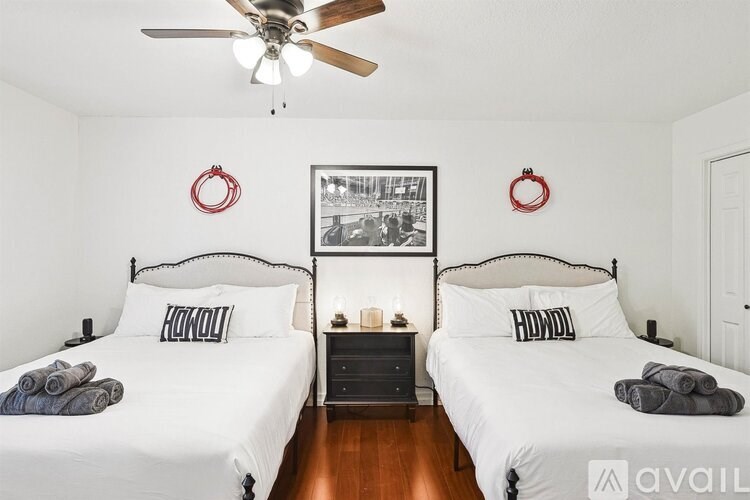 Two identical beds with white bedspreads and pillows, a ceiling fan, and a framed picture on the wall.
