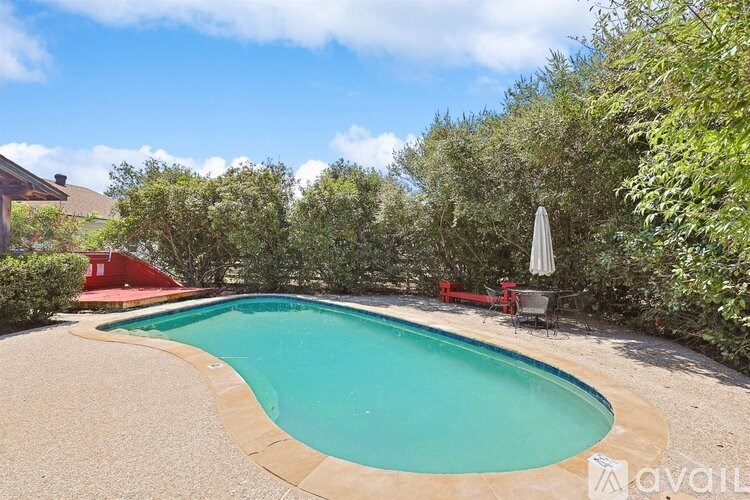 A swimming pool surrounded by greenery and a red bench.