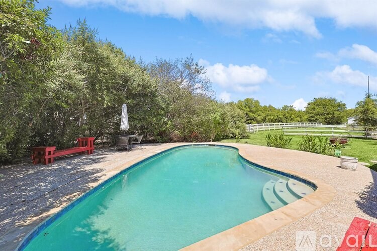 A swimming pool surrounded by trees and a red bench.
