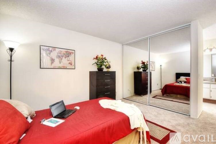A bedroom with a red bed and a laptop on it.