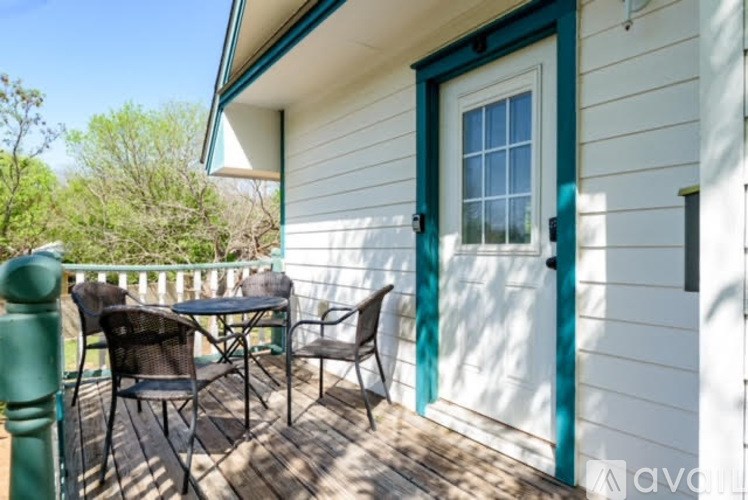 A white house with a green door and a deck with a table and chairs.