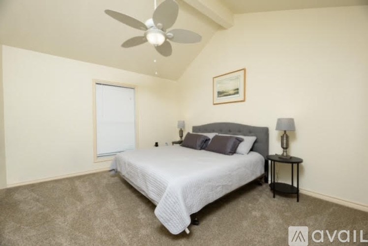 A bedroom with a bed, a fan, and a nightstand.