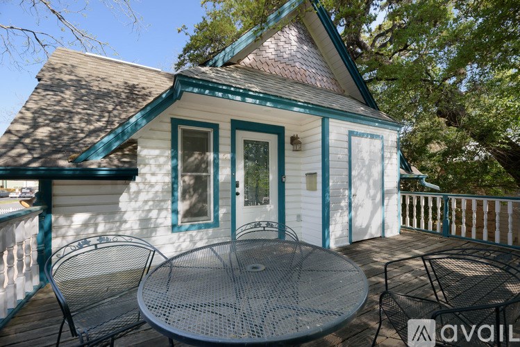 A small white house with a blue roof and a round table on the deck.