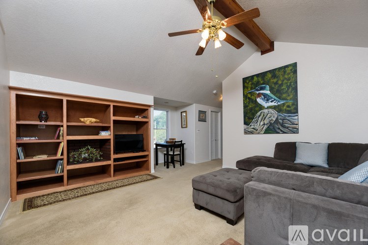 A living room with a grey couch, a wooden bookshelf, and a painting of a bird on the wall.