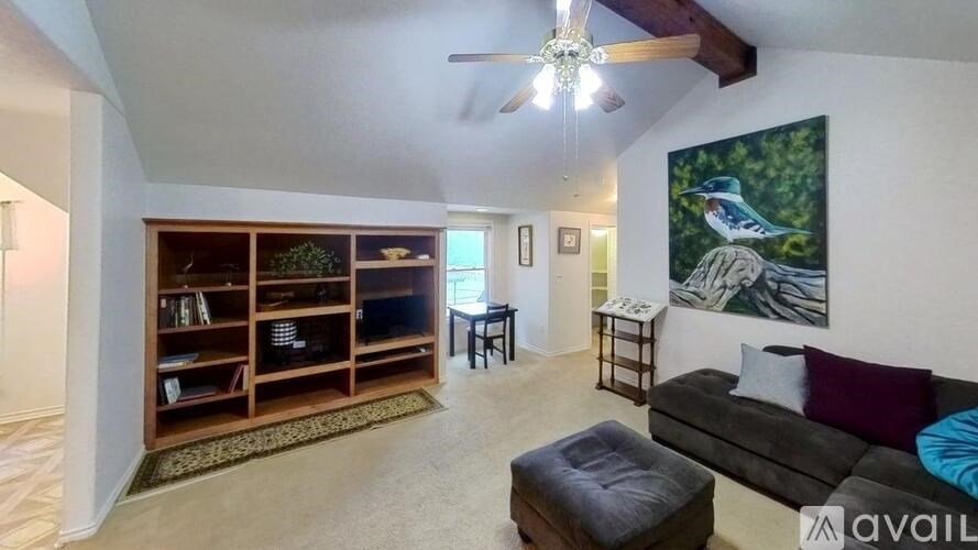 A living room with a couch, a bookshelf, and a painting of a bird.