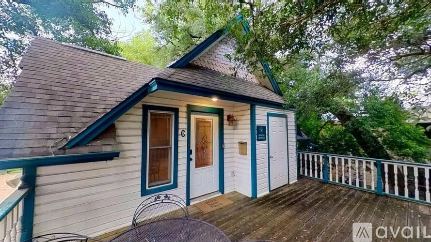 A small house with a porch and a balcony is surrounded by trees.