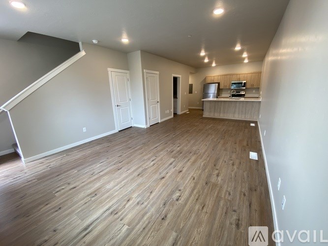 A spacious room with wooden flooring and a staircase on the left side.