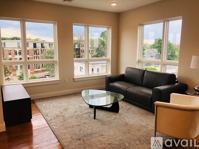 A living room with a black couch, glass table, and a view of a street through the windows.