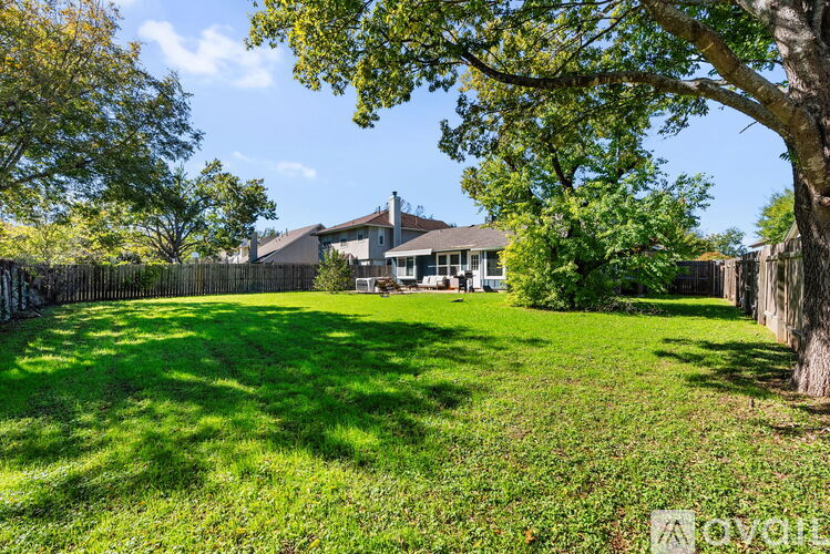 A backyard with a house, trees, and a fence.