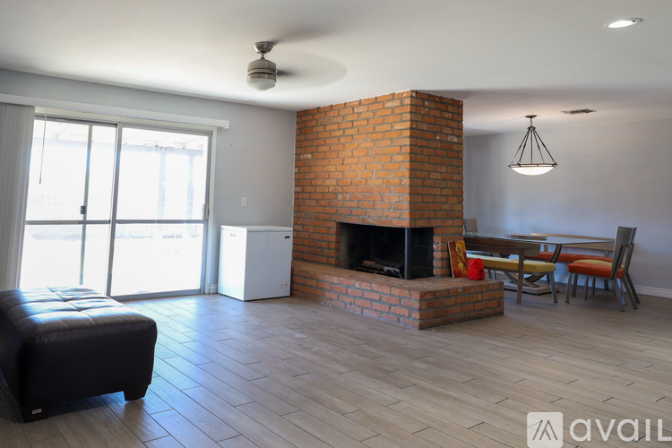 A living room with a brick fireplace and a black leather ottoman.