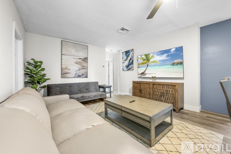 A living room with a white couch and a painting of a beach scene on the wall.