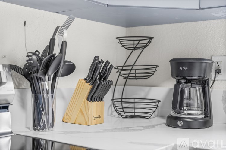 A kitchen counter with a coffee maker, knives, and spoons.