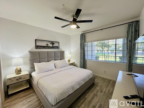 A bedroom with a large bed, a ceiling fan, and a window with a view of the outdoors.