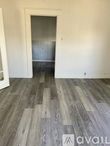 A room with wooden flooring and a doorway leading to another room.