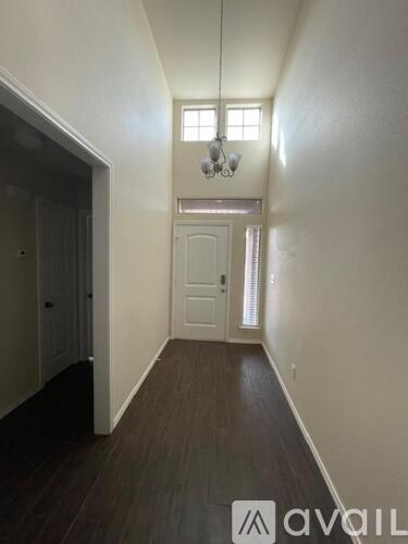 A hallway with wood floors and white walls leading to a door.