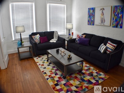 A black couch with a colorful rug in front of it.