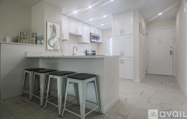 A kitchen with white cabinets and a counter with three stools.