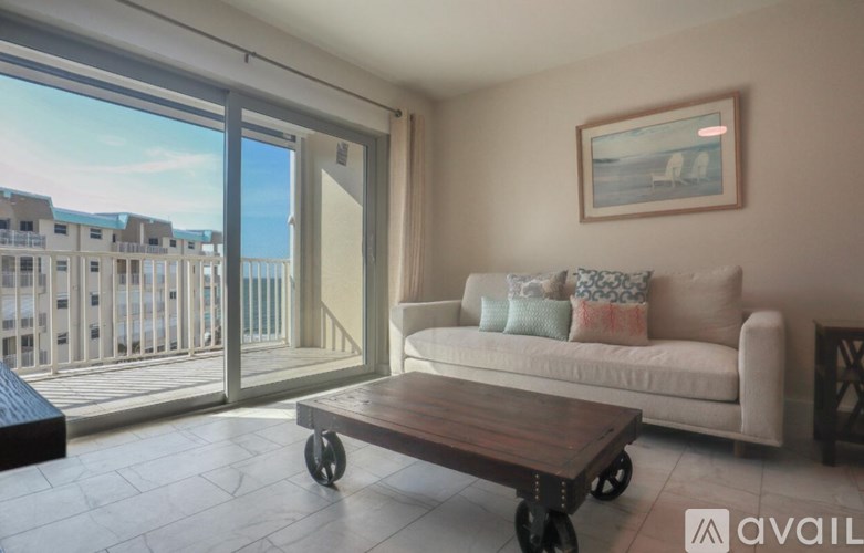 A living room with a couch, coffee table, and a view of a balcony with buildings outside.