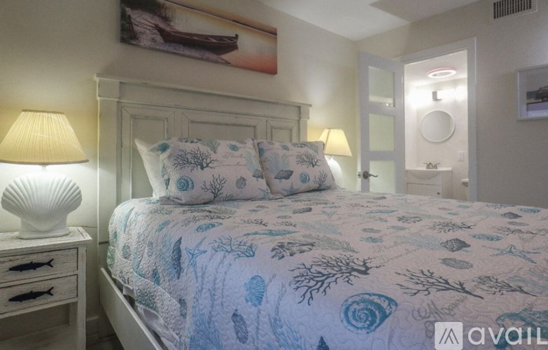 A bed with a blue and white patterned comforter and two matching pillows sits in a room with a lamp and a painting on the wall.