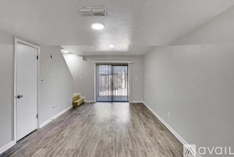 A room with a white door, a window with blinds, and a wooden floor.