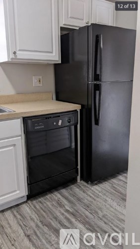 A black refrigerator in a kitchen with white cabinets.