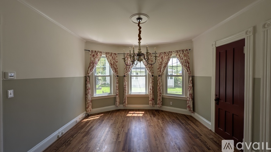 A room with a chandelier, two windows with curtains, and a wooden floor.