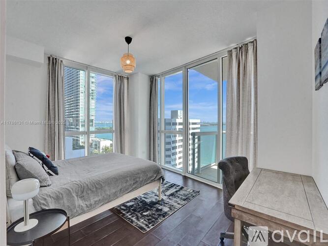 A bedroom with a large bed, a chair, and a table with a view of the city.