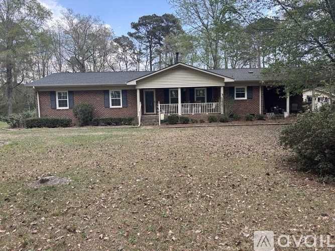 A house with a porch and a covered patio is surrounded by trees and grass.