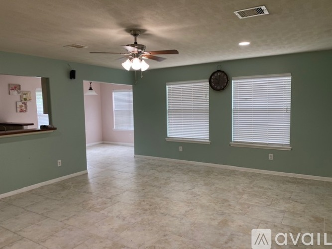 A spacious room with a ceiling fan and two windows with blinds.