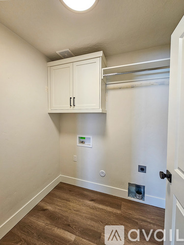 A room with white walls and a wooden floor with a cabinet above it.
